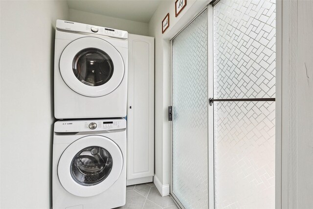 laundry room with stacked washer and dryer, light tile patterned floors, and cabinets