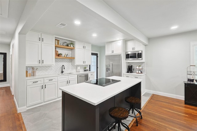 kitchen with appliances with stainless steel finishes, sink, light hardwood / wood-style flooring, white cabinetry, and a breakfast bar area