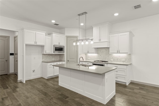 kitchen featuring stainless steel microwave, dark wood-type flooring, a center island with sink, white cabinetry, and hanging light fixtures