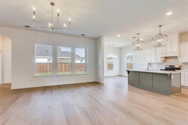 unfurnished living room featuring a wealth of natural light, a chandelier, and light wood-type flooring