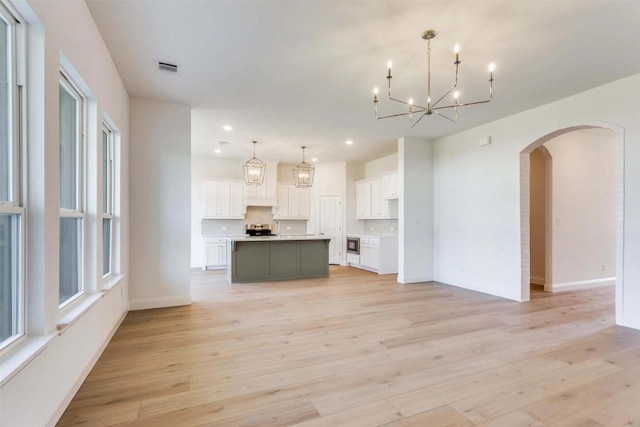 unfurnished living room featuring light wood-type flooring, arched walkways, recessed lighting, and an inviting chandelier