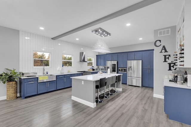 kitchen featuring beam ceiling, sink, a center island, wall chimney range hood, and appliances with stainless steel finishes