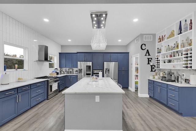 kitchen with stainless steel appliances, a center island, light stone counters, wall chimney exhaust hood, and light wood-type flooring