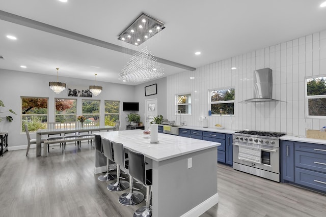 kitchen with a center island, an inviting chandelier, high end stainless steel range oven, wall chimney exhaust hood, and a breakfast bar area