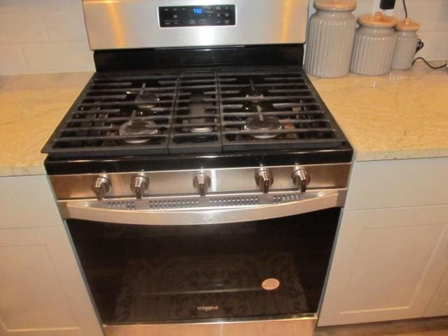 room details featuring white cabinets, decorative backsplash, light stone countertops, and stainless steel gas range oven