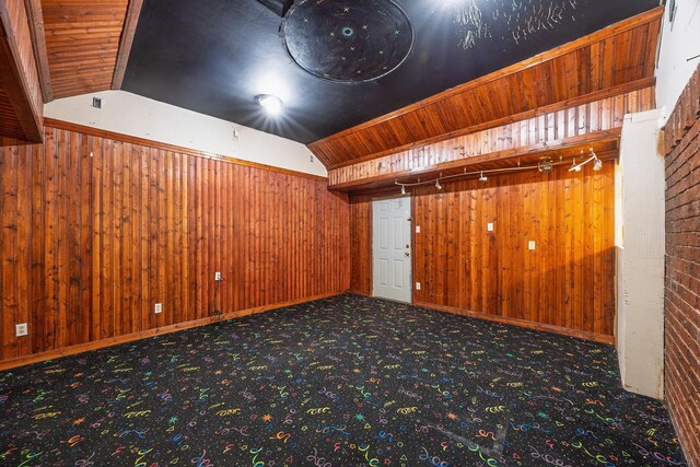 carpeted empty room featuring track lighting, wood walls, wood ceiling, and vaulted ceiling