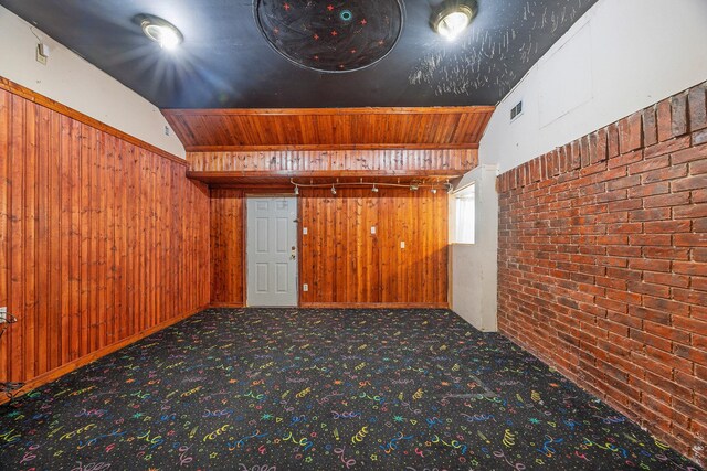 unfurnished room with brick wall, carpet floors, wooden walls, and vaulted ceiling