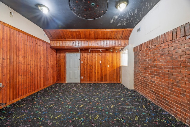 carpeted empty room featuring brick wall, vaulted ceiling, and wood walls