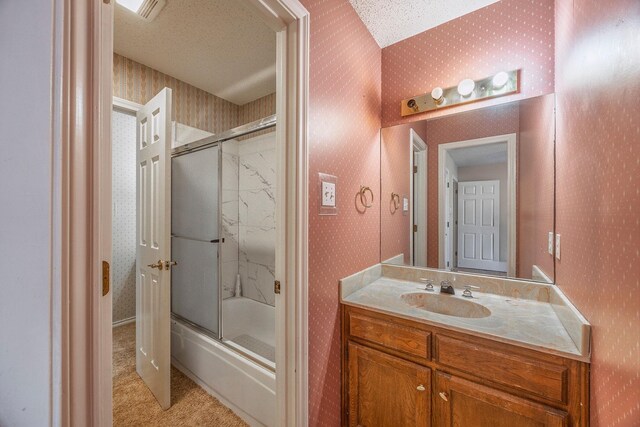 bathroom with vanity, a textured ceiling, and combined bath / shower with glass door