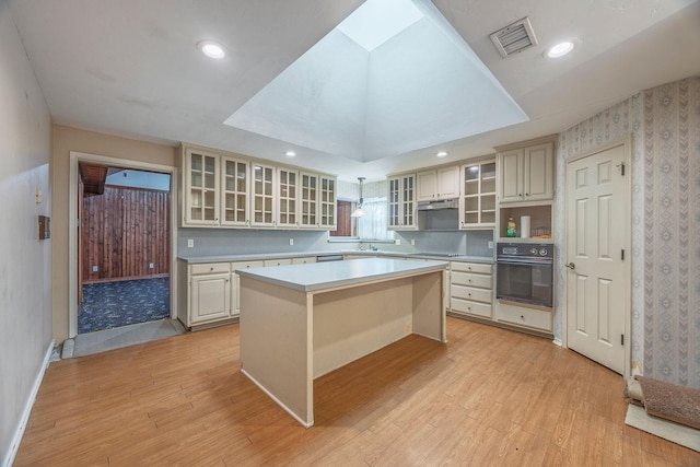 kitchen featuring a center island, a kitchen breakfast bar, light hardwood / wood-style flooring, cream cabinetry, and black appliances