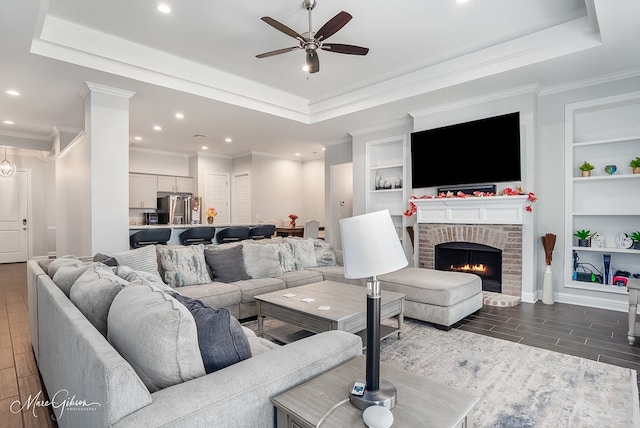 living room with built in shelves, ceiling fan, a fireplace, and a raised ceiling