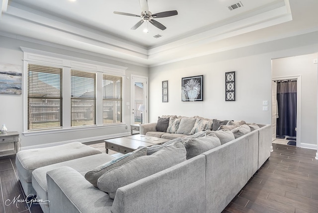 living room with ceiling fan, crown molding, dark wood-type flooring, and a tray ceiling