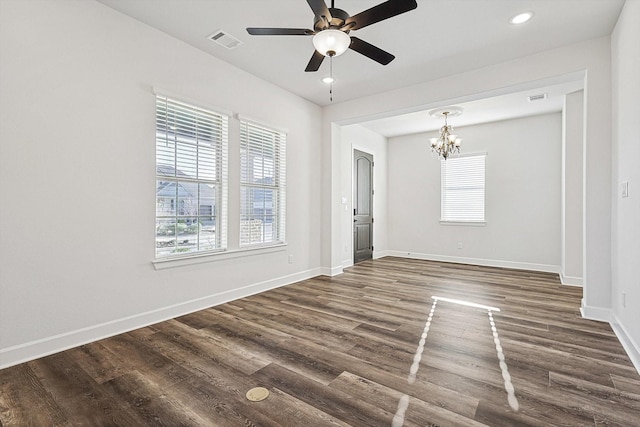 spare room featuring dark hardwood / wood-style flooring, ceiling fan with notable chandelier, and a healthy amount of sunlight