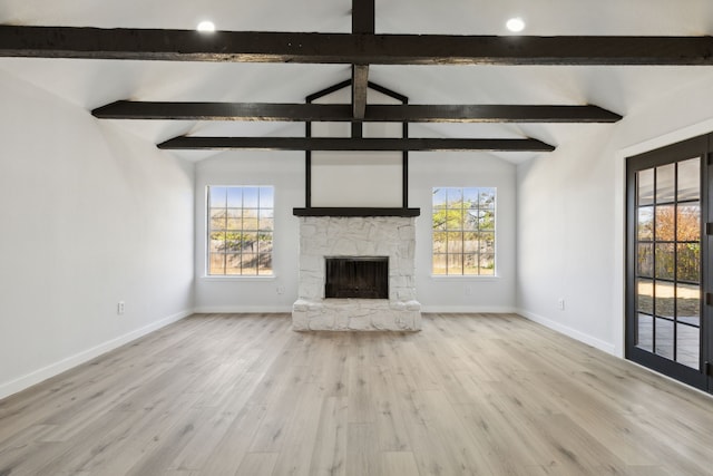 unfurnished living room with vaulted ceiling with beams, plenty of natural light, wood finished floors, and a stone fireplace