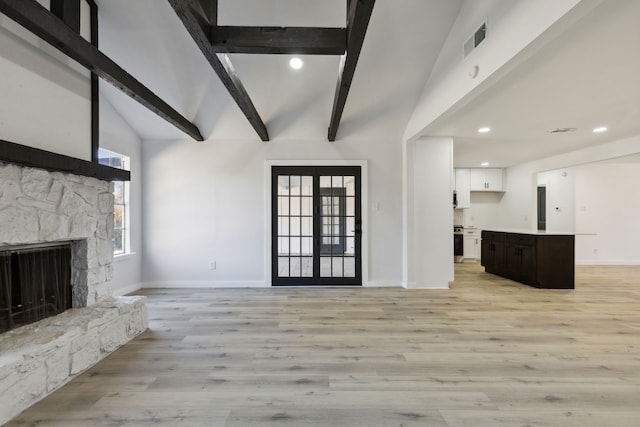 unfurnished living room featuring a stone fireplace, lofted ceiling with beams, and light wood-type flooring