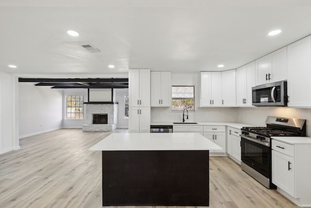 kitchen featuring a stone fireplace, a kitchen island, a sink, appliances with stainless steel finishes, and a wealth of natural light