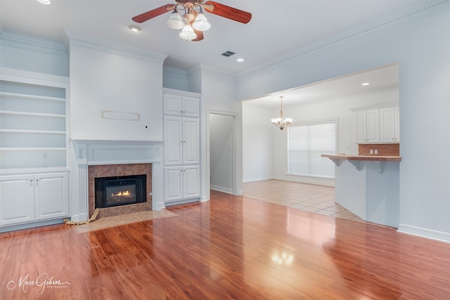 unfurnished living room with crown molding, a fireplace, light hardwood / wood-style floors, and ceiling fan with notable chandelier