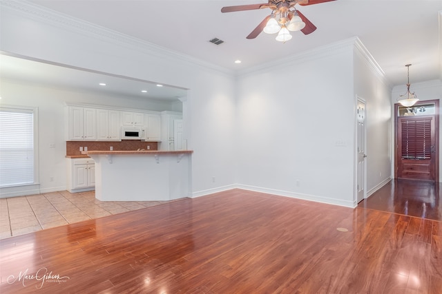 unfurnished living room with ornamental molding, ceiling fan, and light wood-type flooring