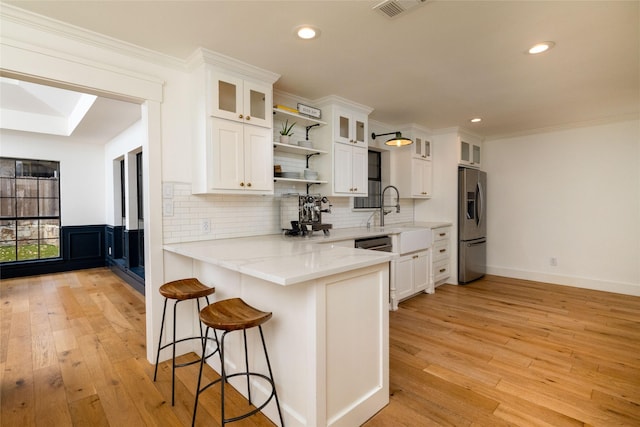 kitchen with white cabinetry, a kitchen breakfast bar, stainless steel fridge with ice dispenser, kitchen peninsula, and crown molding