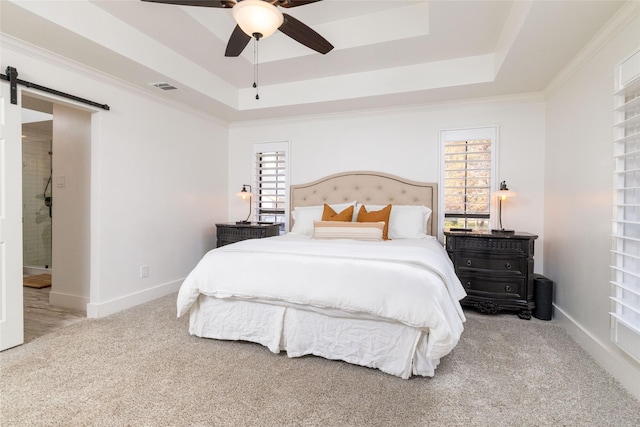 carpeted bedroom with ceiling fan, ornamental molding, a tray ceiling, and a barn door