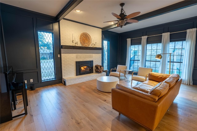 living room featuring ceiling fan, a brick fireplace, ornamental molding, light hardwood / wood-style floors, and beamed ceiling