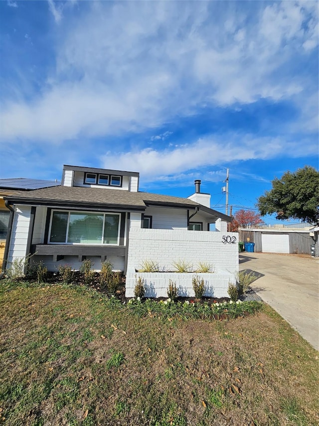 view of front of home with an outdoor structure, a garage, a front yard, and solar panels