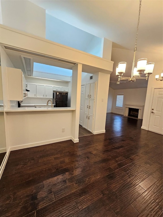 kitchen with white cabinetry, black fridge, dark hardwood / wood-style flooring, decorative light fixtures, and kitchen peninsula