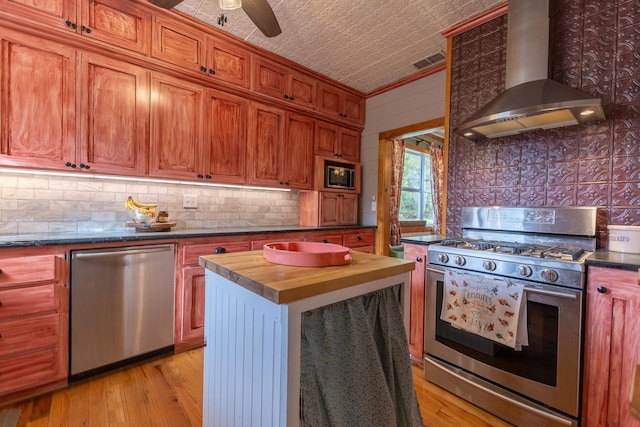 kitchen with wall chimney exhaust hood, wooden counters, light wood-type flooring, stainless steel appliances, and decorative backsplash