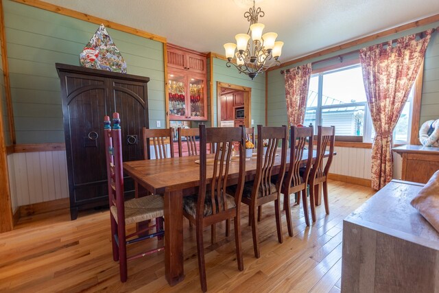 dining room featuring wooden walls, light hardwood / wood-style floors, and an inviting chandelier