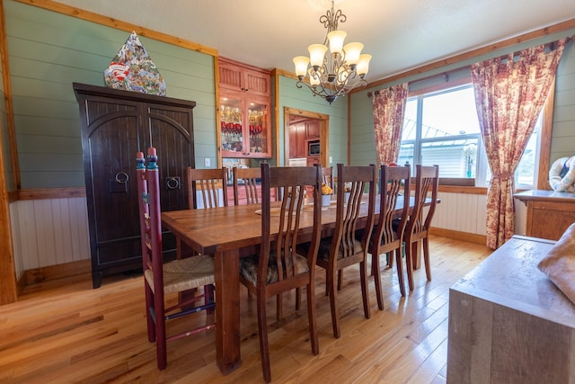 dining space with an inviting chandelier, wood walls, and light wood-type flooring