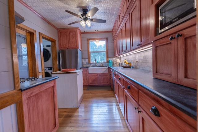 kitchen with sink, crown molding, appliances with stainless steel finishes, stacked washer / dryer, and light wood-type flooring