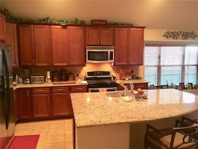 kitchen featuring sink, light stone counters, an island with sink, light tile patterned floors, and appliances with stainless steel finishes