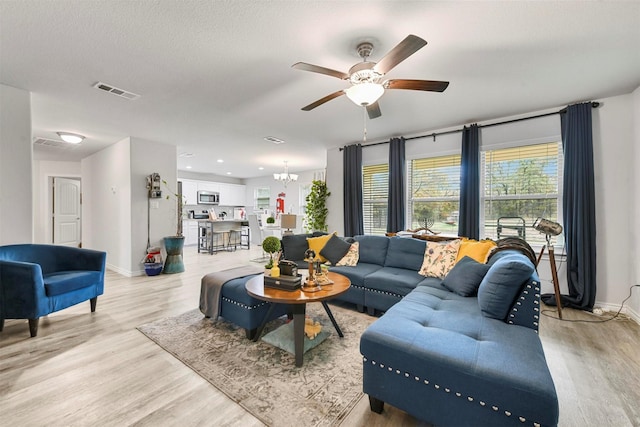 living room with ceiling fan with notable chandelier, a textured ceiling, and light hardwood / wood-style floors