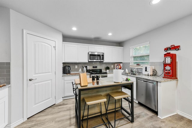 kitchen with a center island, light hardwood / wood-style flooring, light stone counters, white cabinetry, and stainless steel appliances