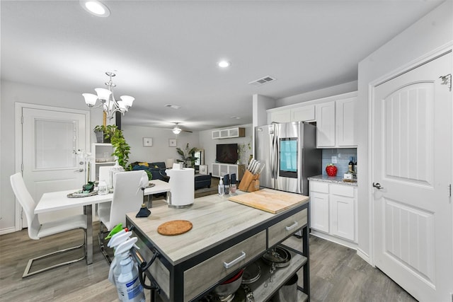 kitchen with stainless steel refrigerator with ice dispenser, ceiling fan with notable chandelier, dark wood-type flooring, white cabinets, and hanging light fixtures