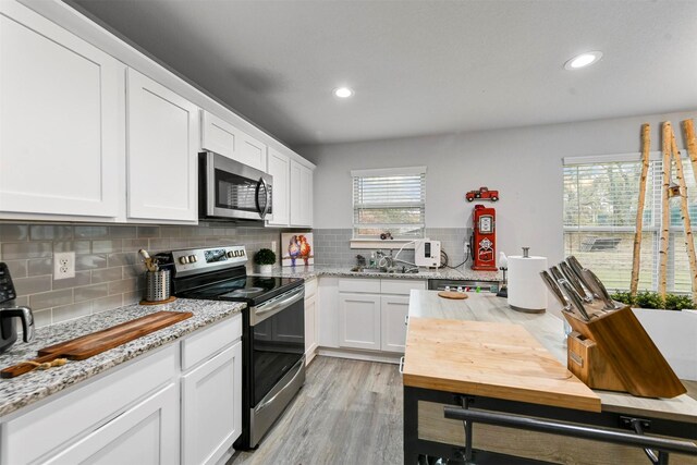 kitchen with light stone countertops, light wood-type flooring, backsplash, stainless steel appliances, and white cabinetry