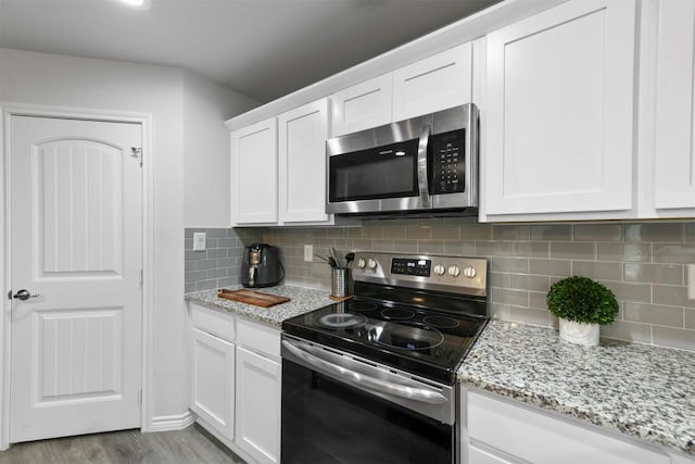 kitchen with backsplash, white cabinets, light stone countertops, light wood-type flooring, and appliances with stainless steel finishes