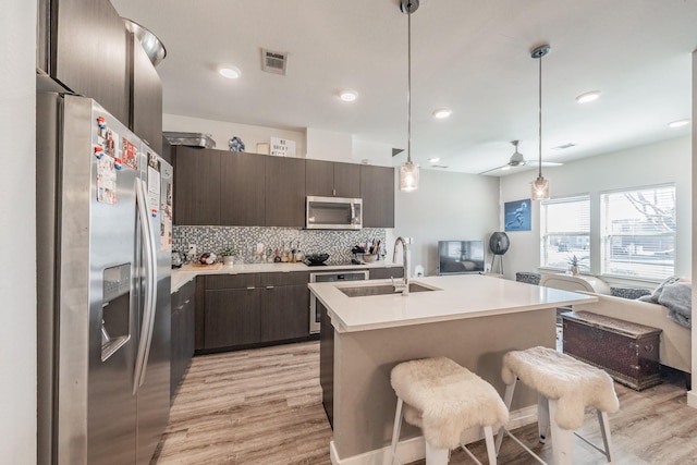 kitchen with open floor plan, stainless steel appliances, dark brown cabinets, and a sink