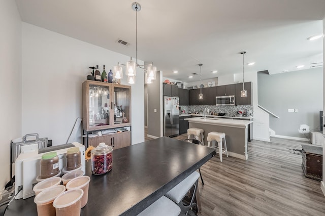 kitchen with stainless steel appliances, visible vents, light countertops, backsplash, and an island with sink