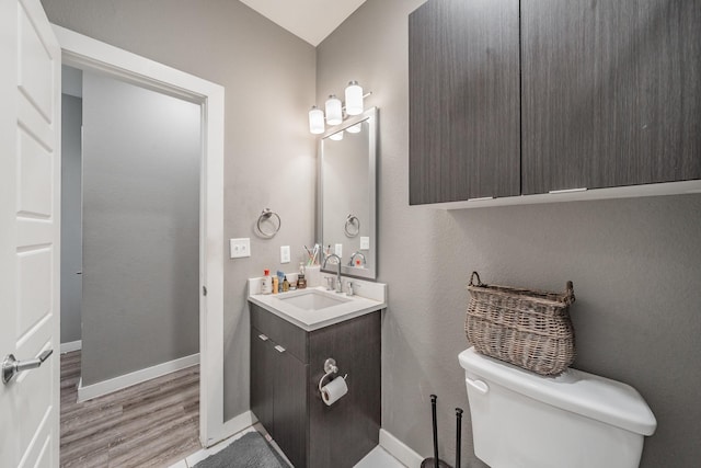 half bathroom with vanity, wood finished floors, toilet, and baseboards