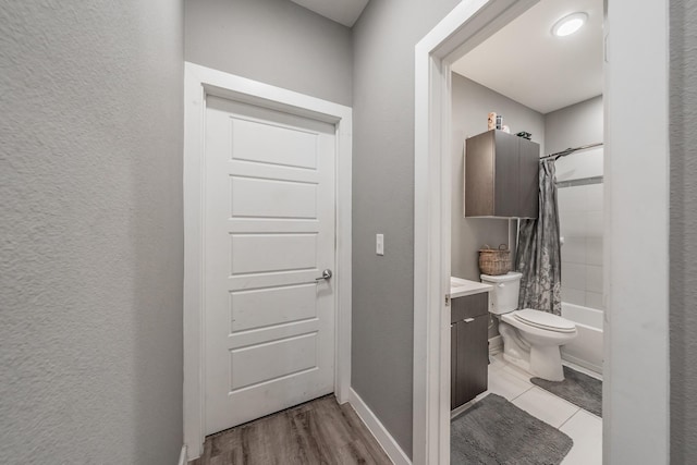 bathroom with toilet, wood finished floors, vanity, baseboards, and shower / bath combo