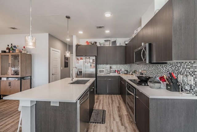 kitchen with stainless steel appliances, visible vents, light wood-style flooring, decorative backsplash, and a sink