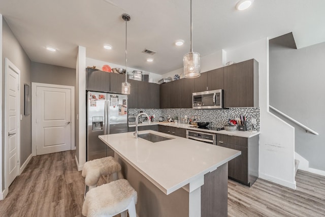 kitchen with light countertops, decorative backsplash, appliances with stainless steel finishes, a sink, and dark brown cabinetry