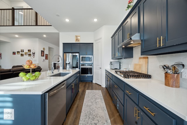 kitchen featuring appliances with stainless steel finishes, blue cabinets, an island with sink, sink, and dark wood-type flooring