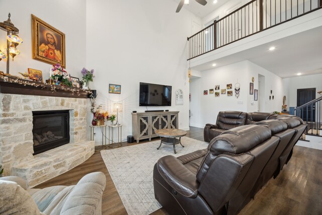 living room with ceiling fan, dark hardwood / wood-style floors, a stone fireplace, and a towering ceiling