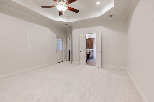 unfurnished bedroom featuring ceiling fan, ensuite bathroom, ornamental molding, light colored carpet, and a raised ceiling