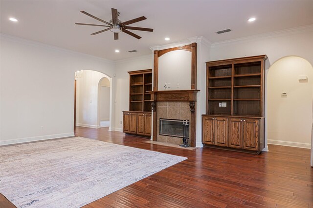 unfurnished living room with ceiling fan, crown molding, dark wood-type flooring, and a tile fireplace