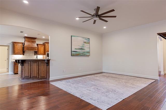 unfurnished living room with dark hardwood / wood-style floors, ceiling fan, crown molding, and sink