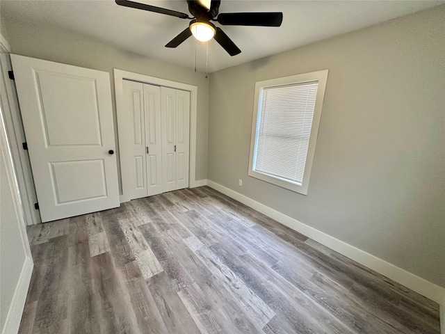 unfurnished bedroom with a closet, wood finished floors, a ceiling fan, and baseboards