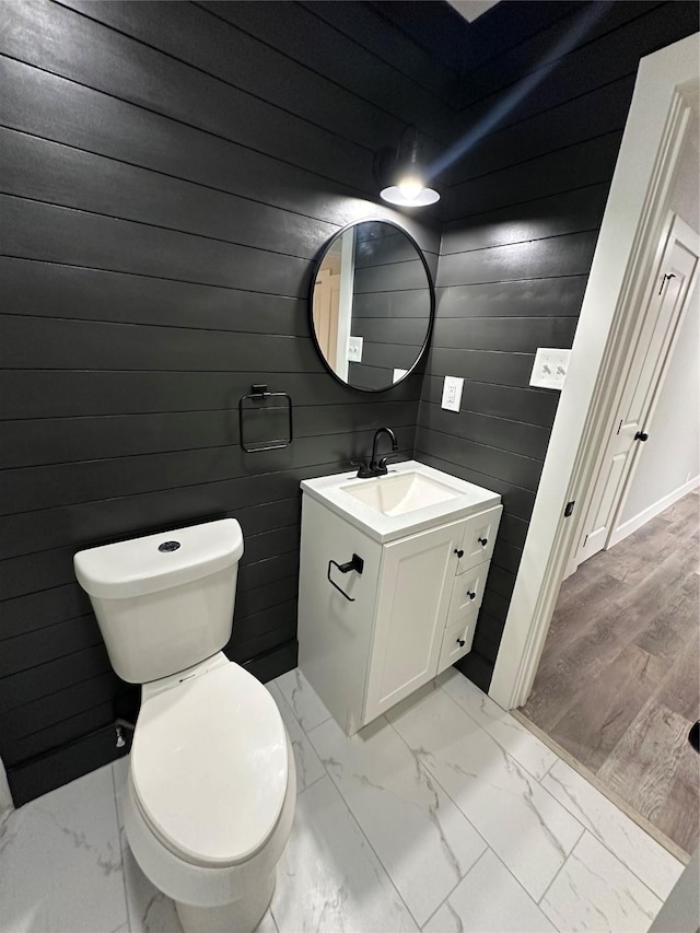 bathroom featuring toilet, marble finish floor, wood walls, and vanity